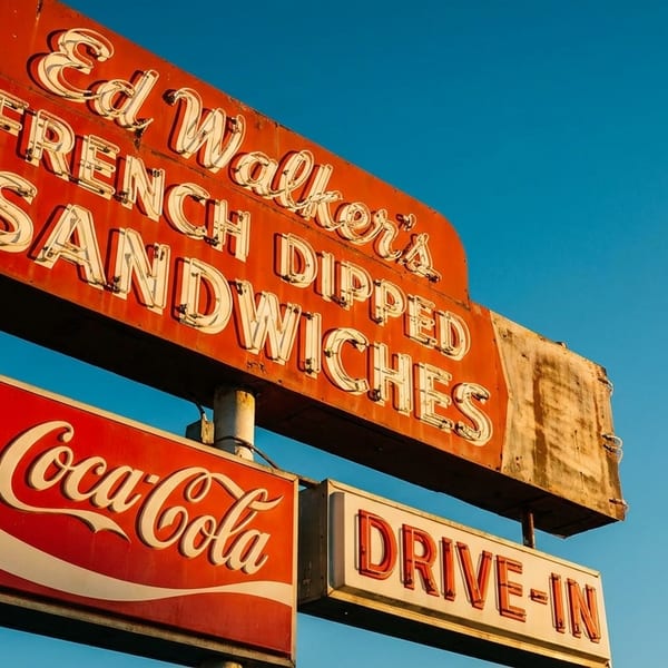 A vintage red neon sign for "Ed Walker's French Dipped Sandwiches" and "Coca-Cola Drive-In" against a blue sky.