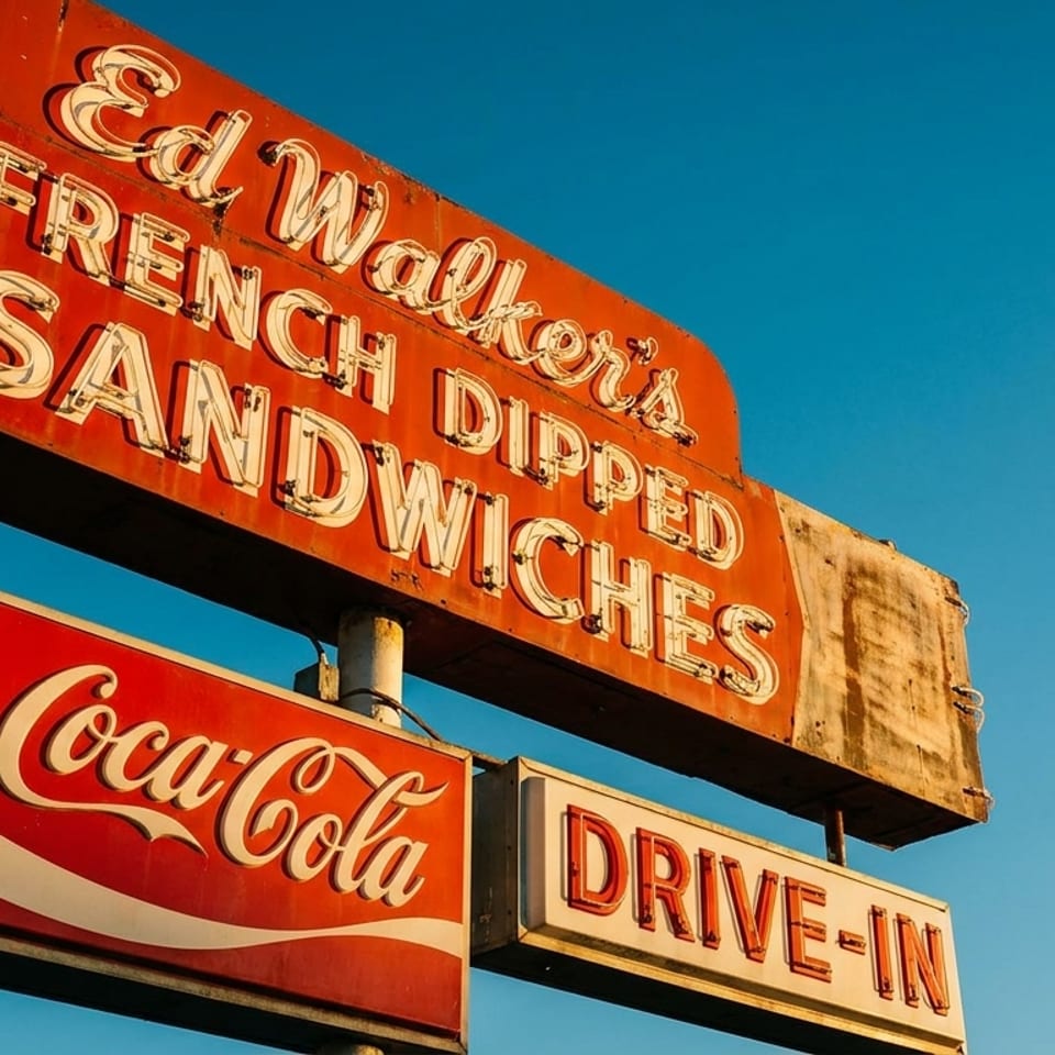 A vintage red neon sign for "Ed Walker's French Dipped Sandwiches" and "Coca-Cola Drive-In" against a blue sky.