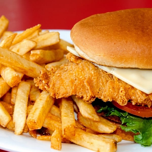 Crispy fried chicken sandwich with cheese, lettuce, and tomato, served with golden french fries.