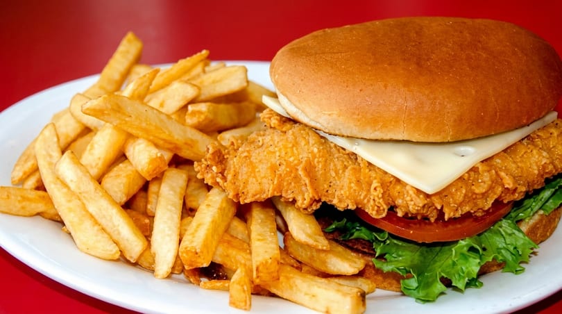 Crispy fried chicken sandwich with cheese, lettuce, and tomato, served with golden french fries.